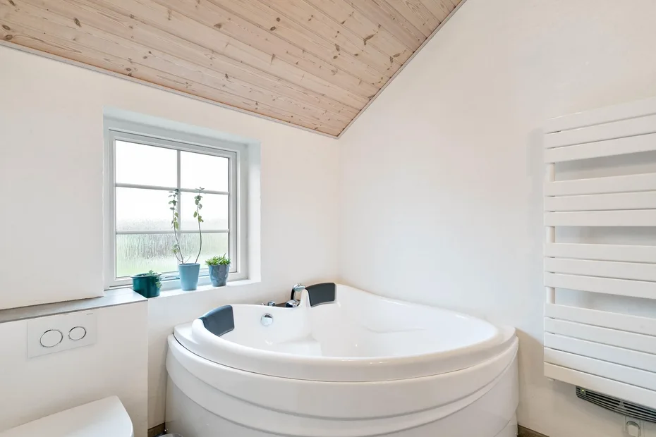 Un baño con una bañera de esquina bajo un techo inclinado de madera.