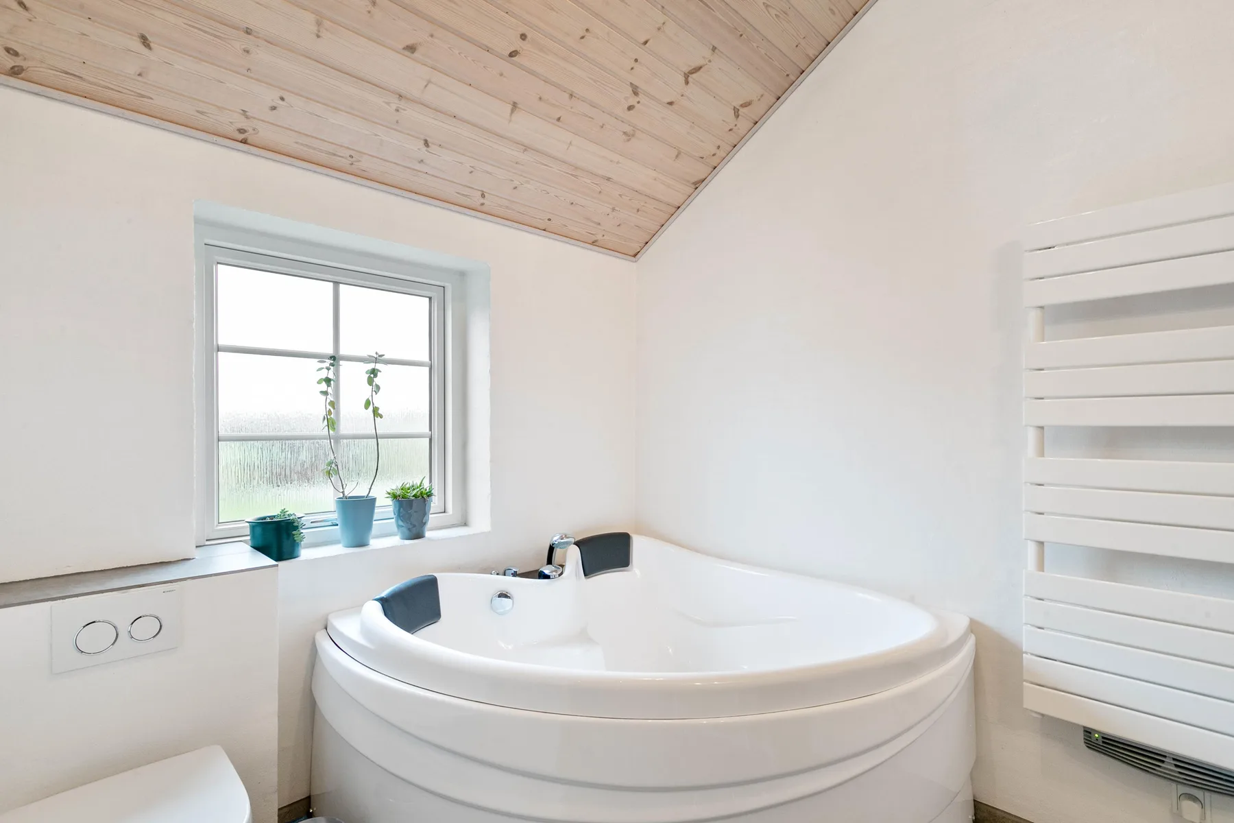 Un baño luminoso con una bañera de esquina junto a una ventana.