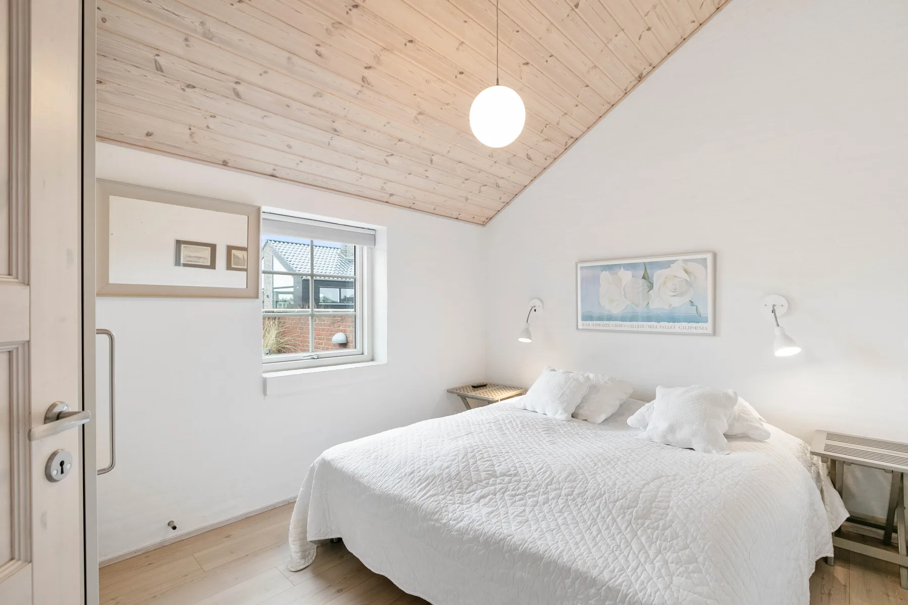Dormitorio luminoso con una cama bien tendida y techo inclinado de madera.