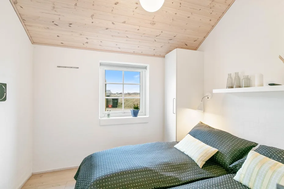 Un dormitorio luminoso con una ventana y una cama con ropa de cama estampada.