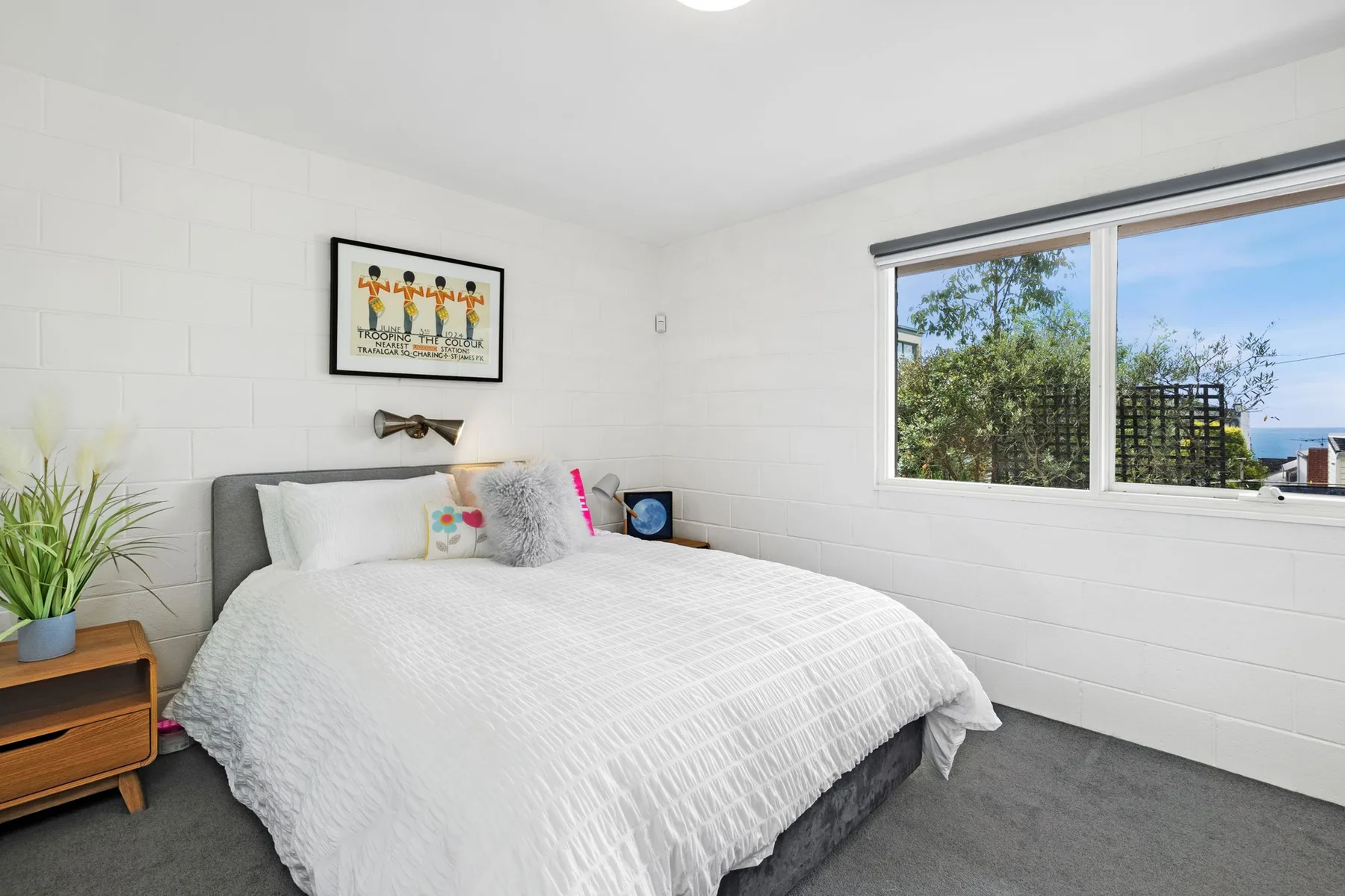 Un dormitorio luminoso con una cama tendida junto a una ventana grande.
