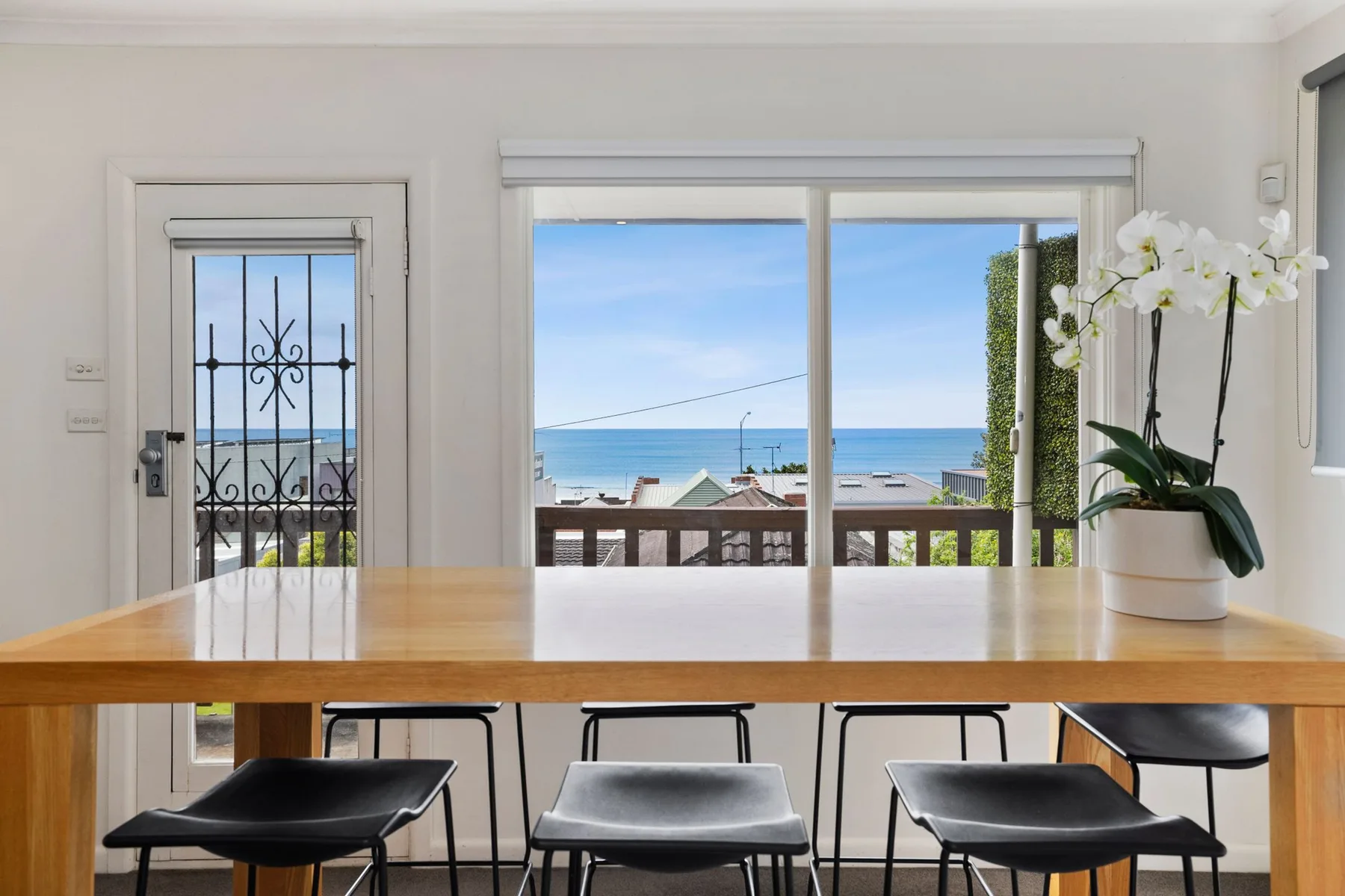 A dining area with a wooden table, chairs, and ocean views through the windows.