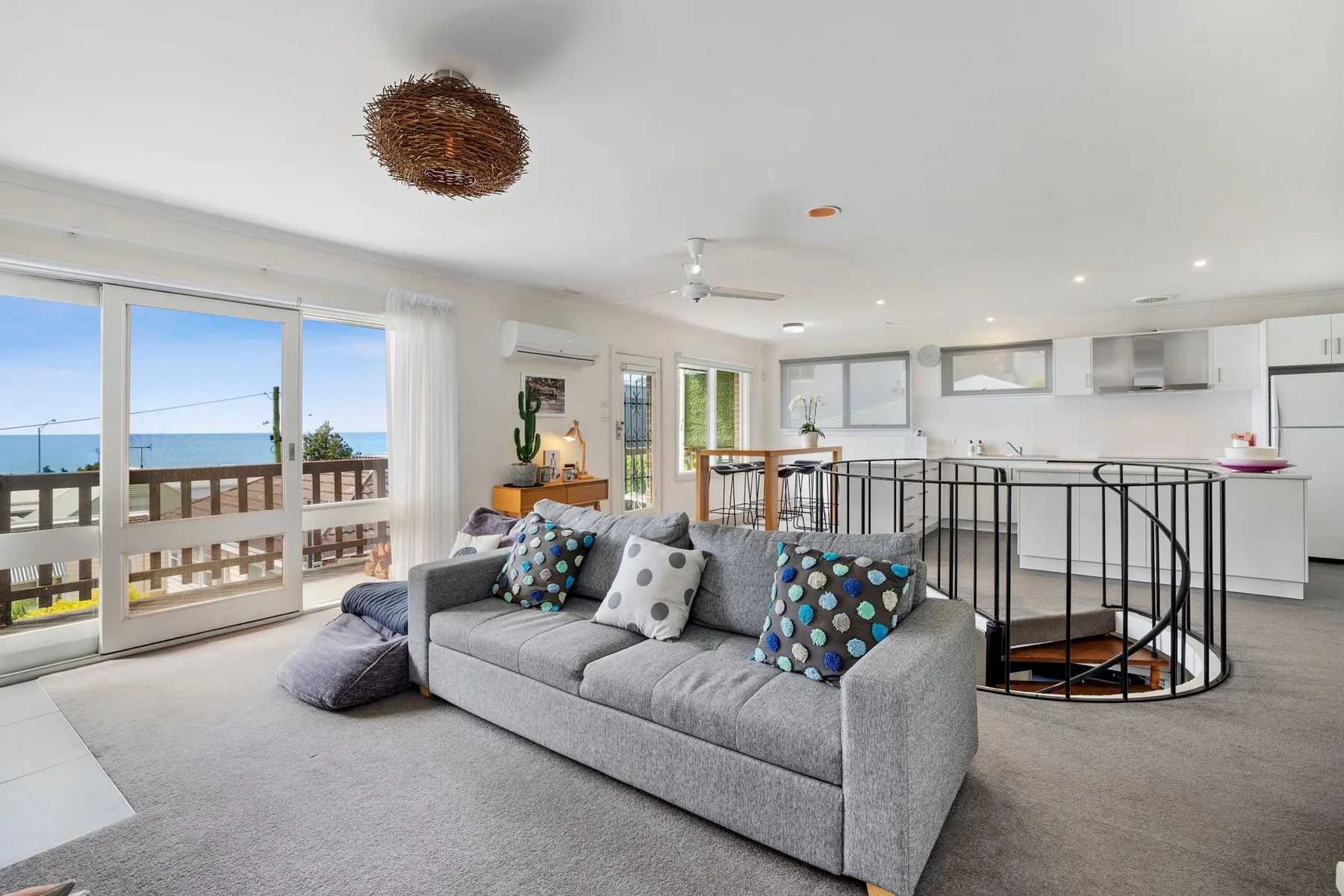 Open-plan living room with gray seating beside a bright kitchen.