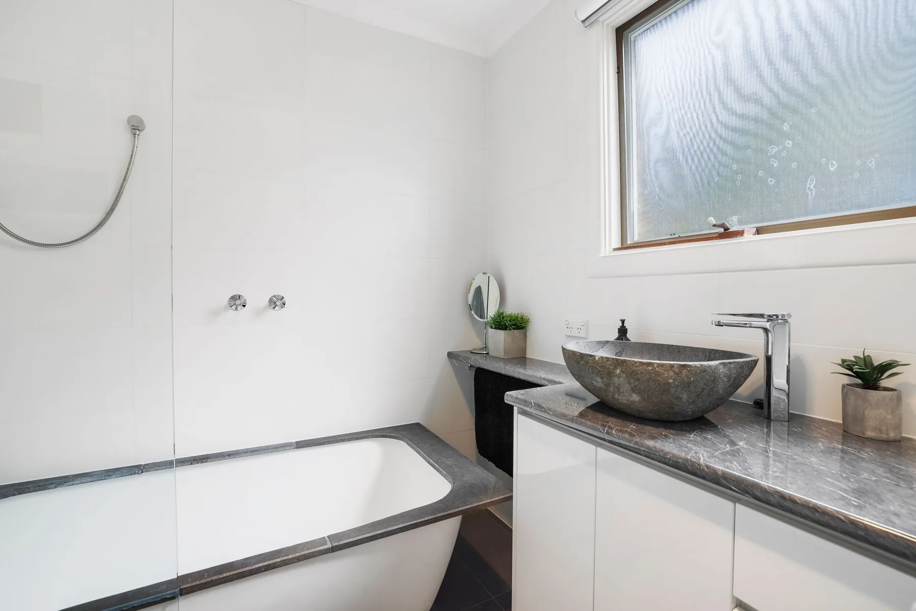 Un baño luminoso con bañera y lavabo sobre encimera bajo una ventana.