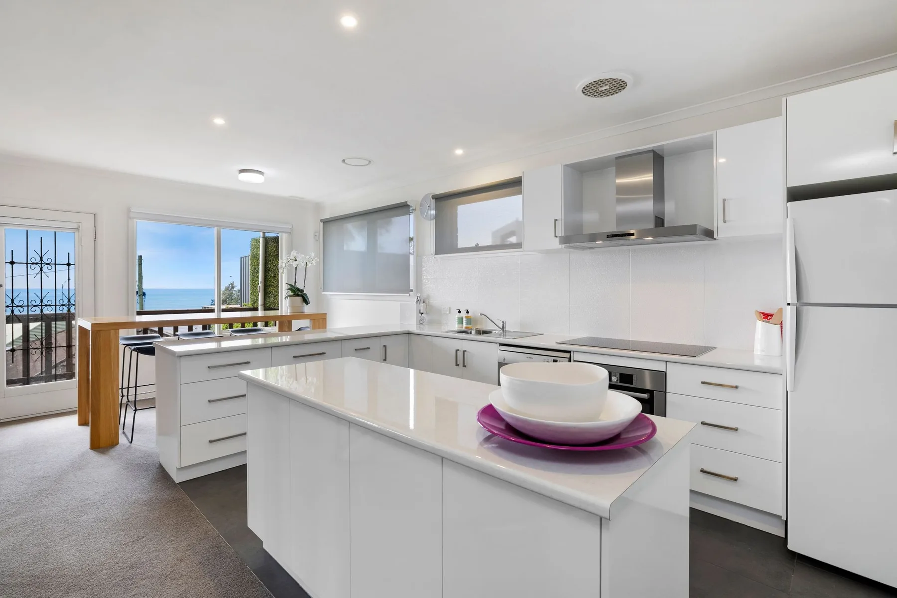 A bright modern kitchen with a central island and ocean views through the windows.