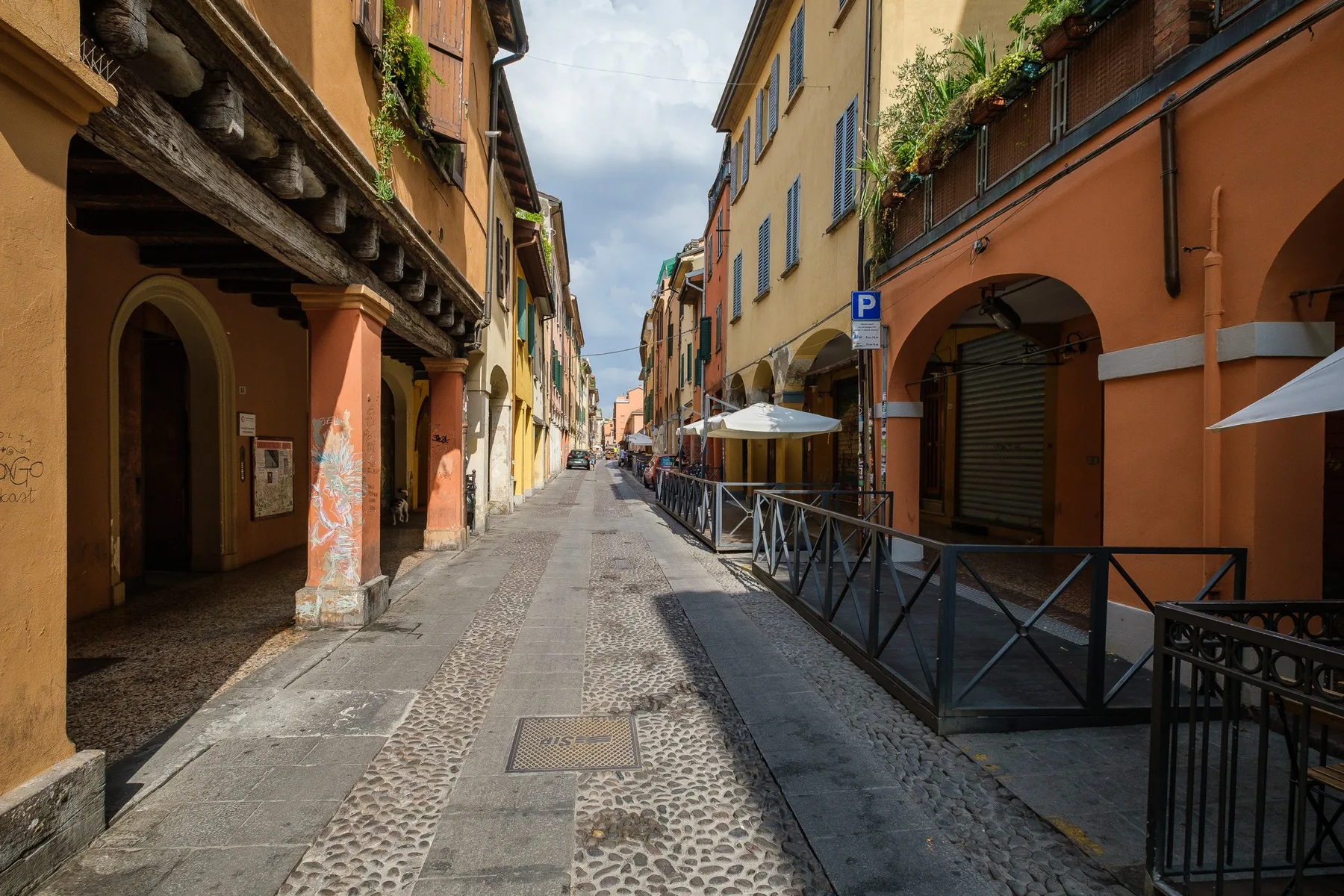 Una calle estrecha flanqueada por edificios coloridos y mesas de café al aire libre.