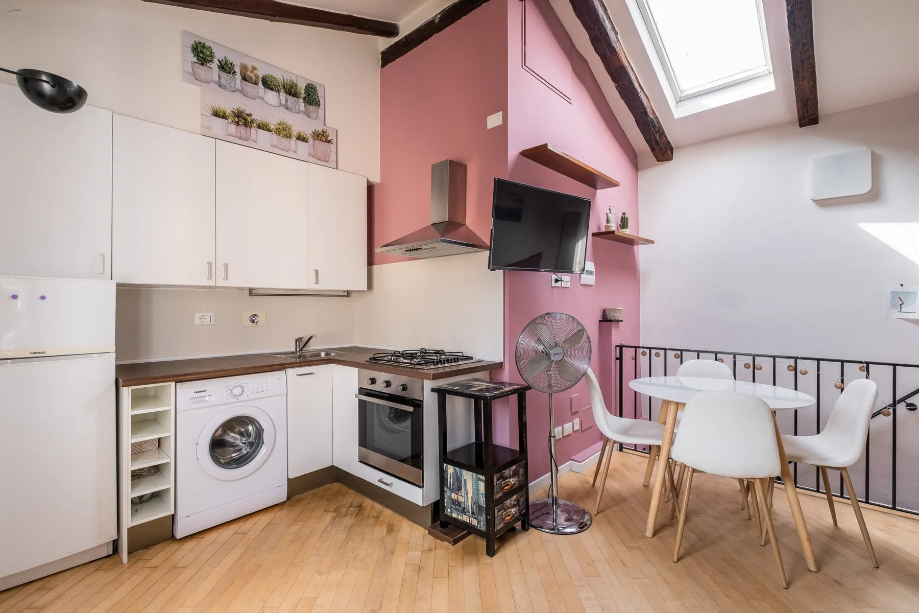 Una cocina compacta con zona de comedor, armarios blancos y una mesa.
