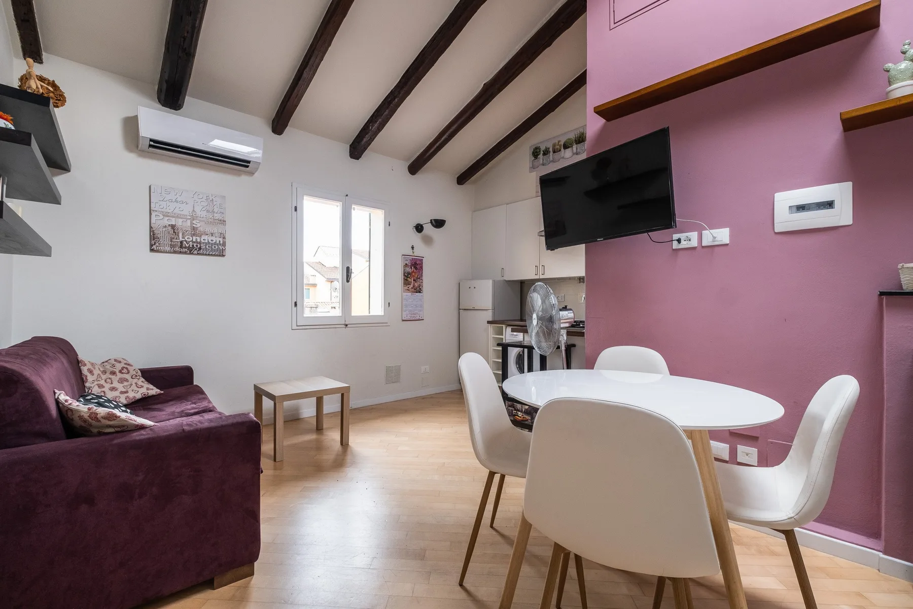 Sala de estar y comedor con asientos, una mesa y un televisor en la pared.