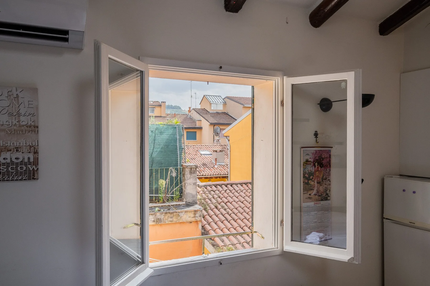 Una ventana abierta da a edificios vecinos de colores y tejados de tejas.