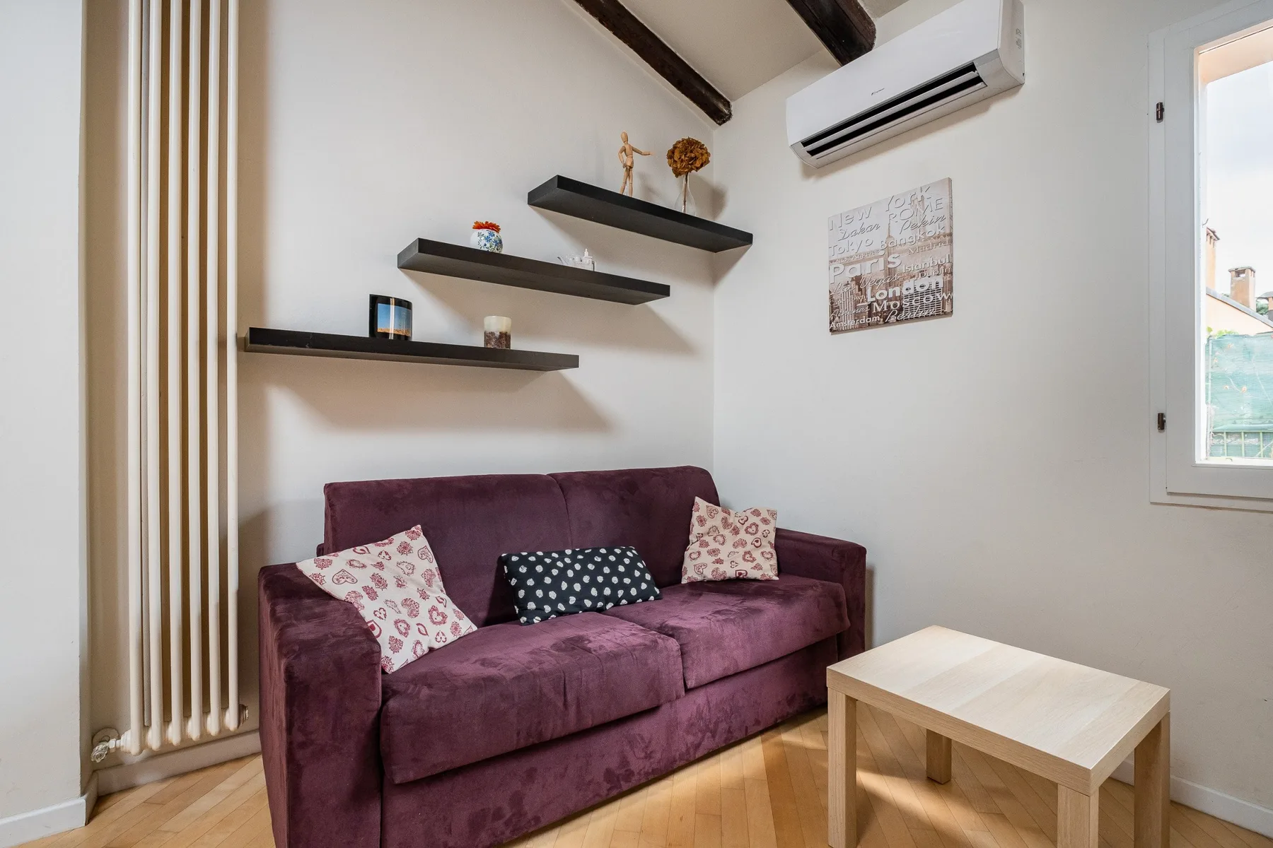 Una sala de estar con asientos morados, estantes de pared y una pequeña mesa de madera.