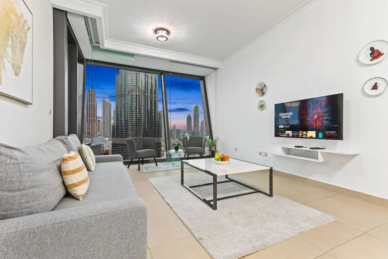 Una sala luminosa con asientos, una mesa de centro y grandes ventanas con vistas a edificios de la ciudad.