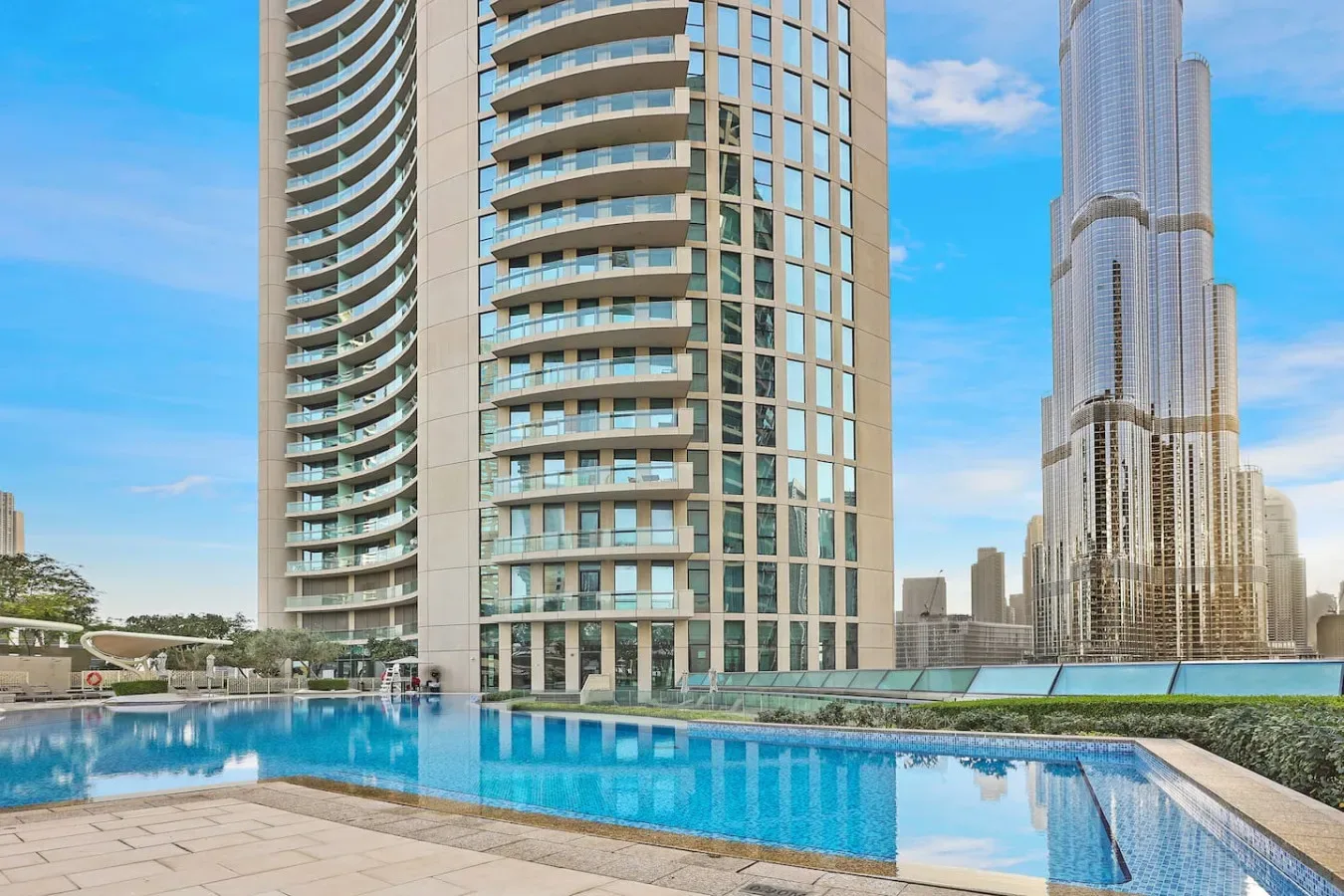 Una piscina en la azotea está junto a modernos edificios altos bajo un cielo azul.