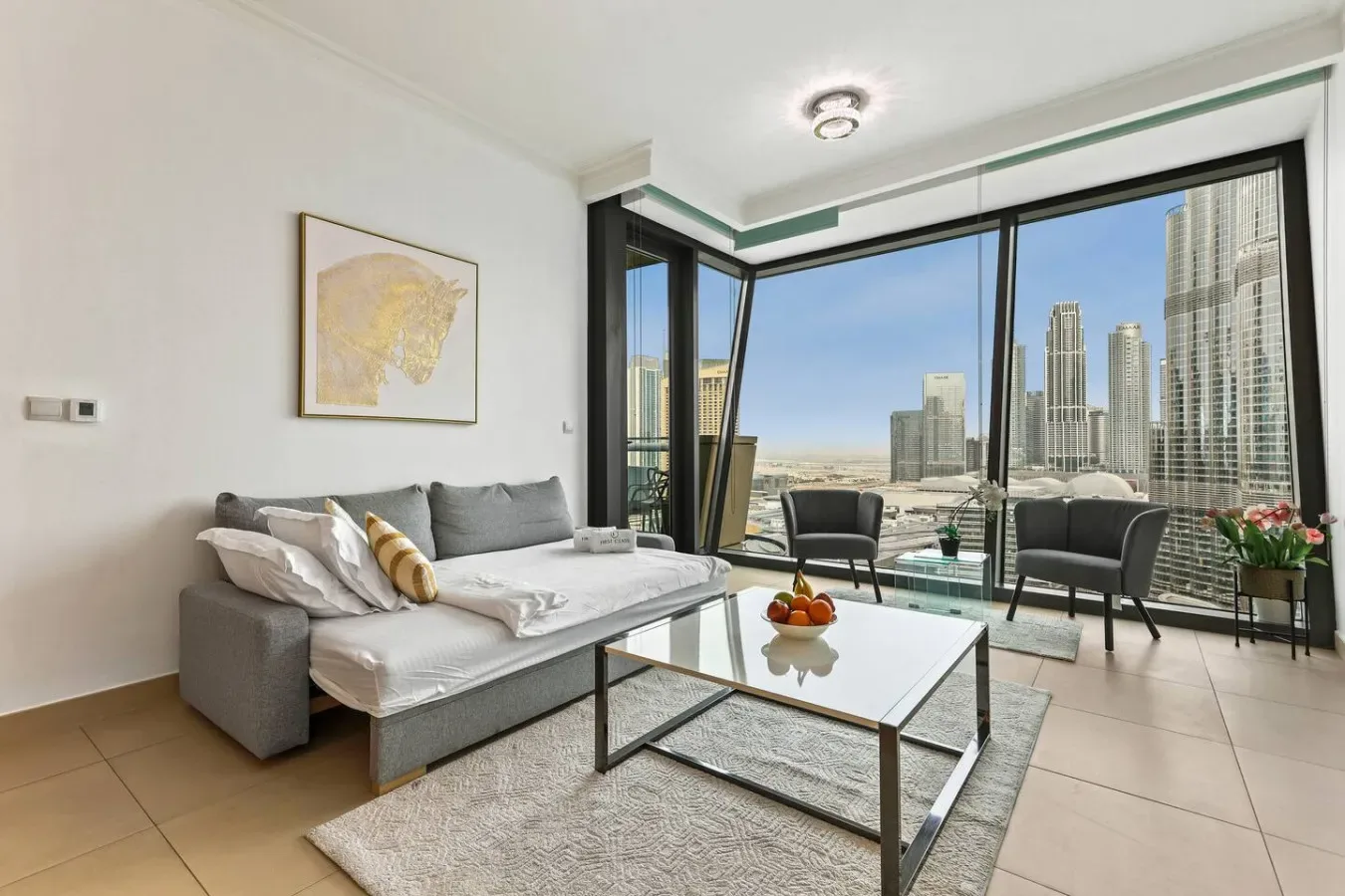 A bright living room with seating, a coffee table, and large windows overlooking city towers.