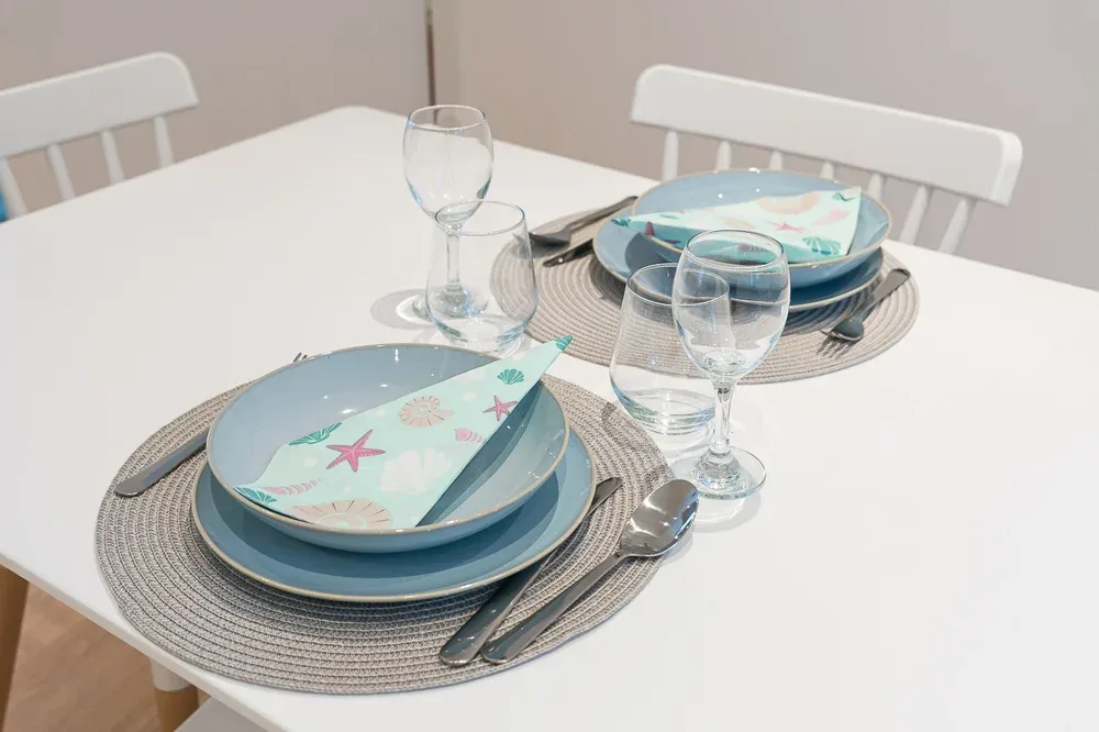 A dining table is set with blue plates, patterned napkins, and drinking glasses.