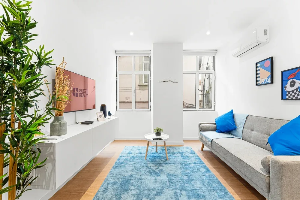 A bright living room with a gray sofa, blue rug, and wall-mounted television.