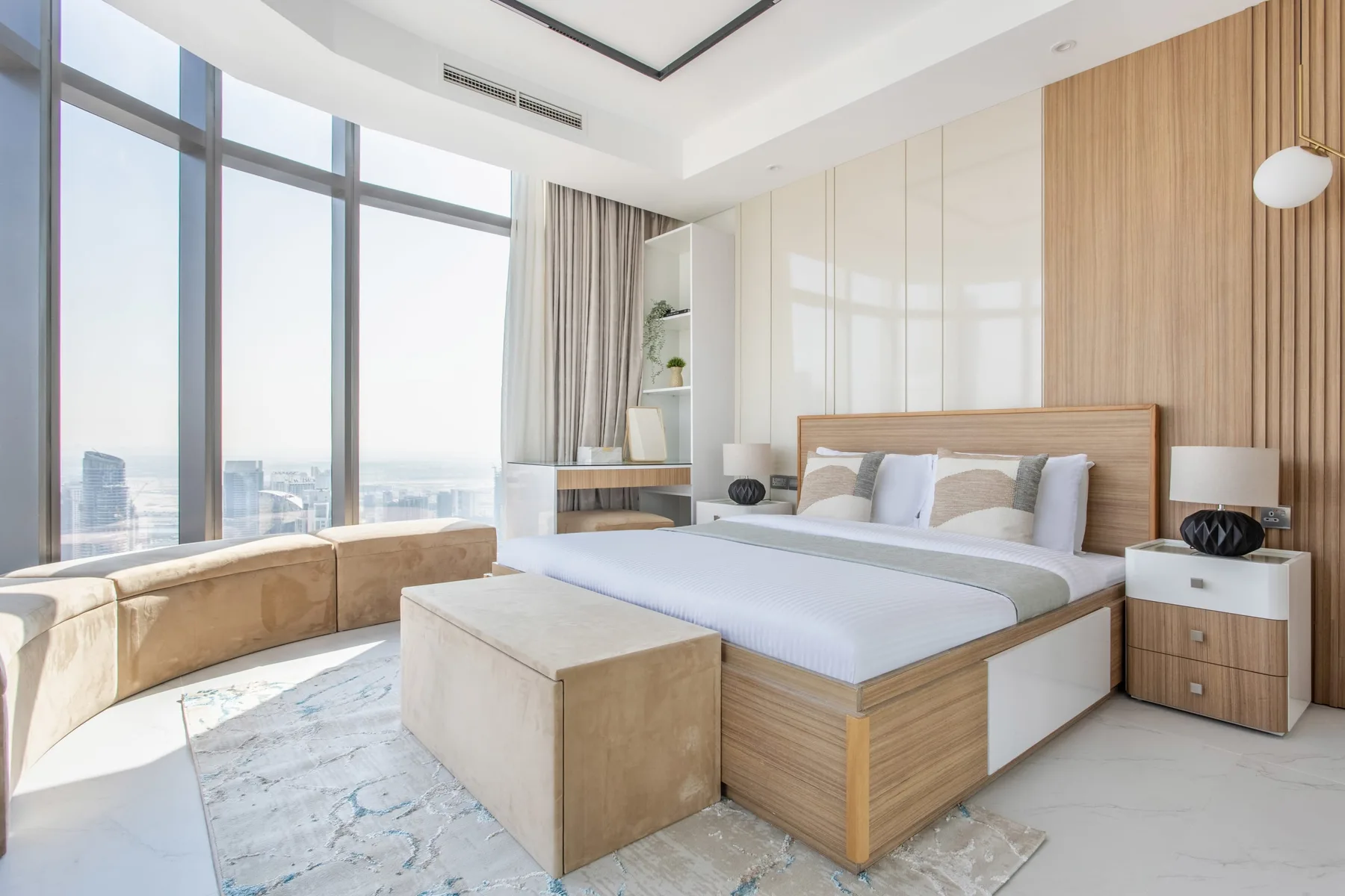 A bright bedroom with a bed, large windows, and a small seating area.