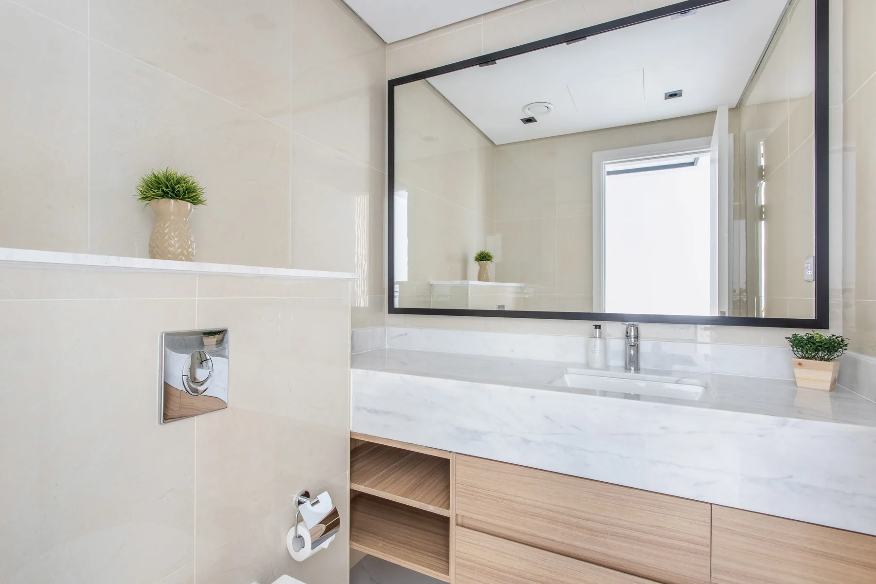 A bright bathroom with a wide vanity, sink, and large wall mirror.