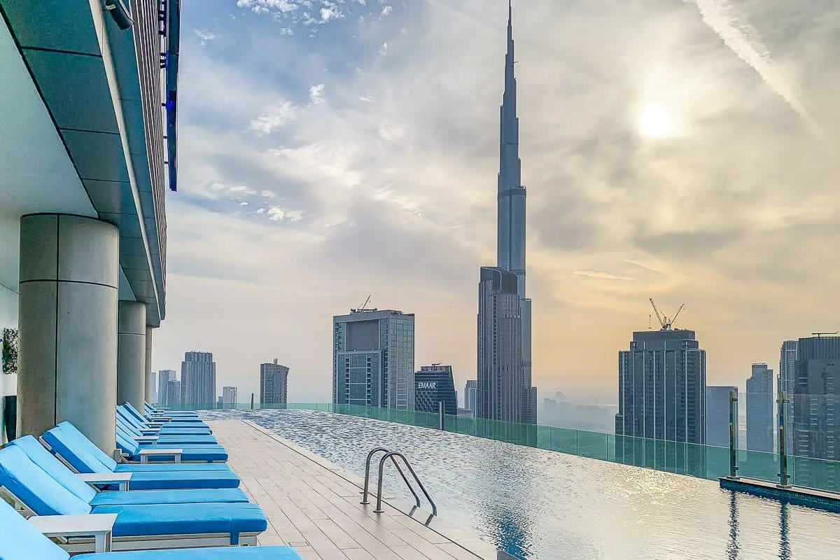 An infinity pool overlooks a city skyline, with blue loungers along the deck.