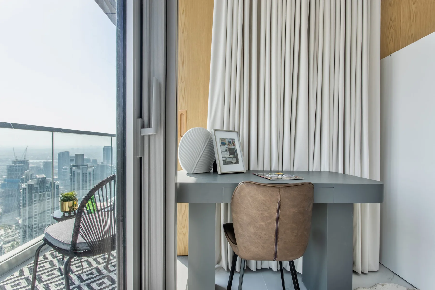 A desk and chair sit beside a large window overlooking the city.