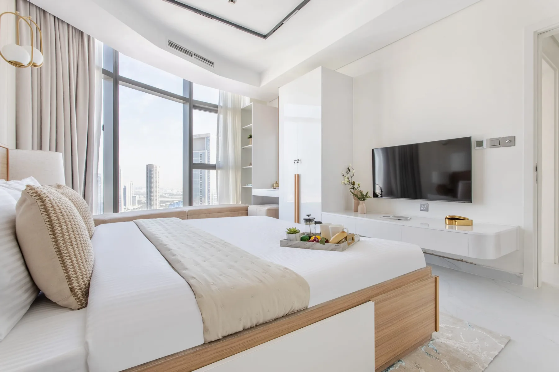A bright bedroom with a bed beside large windows and a wall-mounted television.