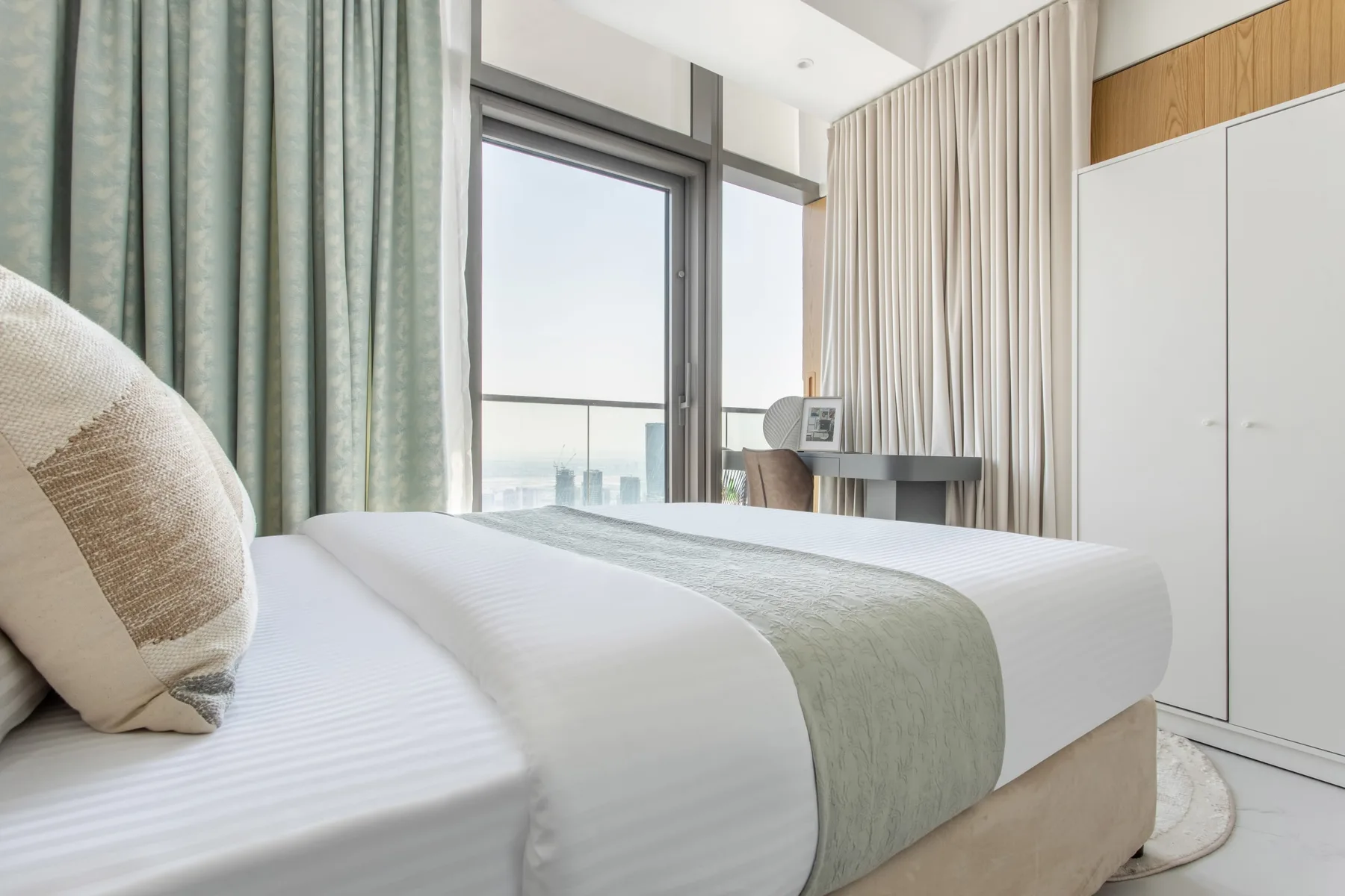 A bedroom with a neatly made bed and tall windows.
