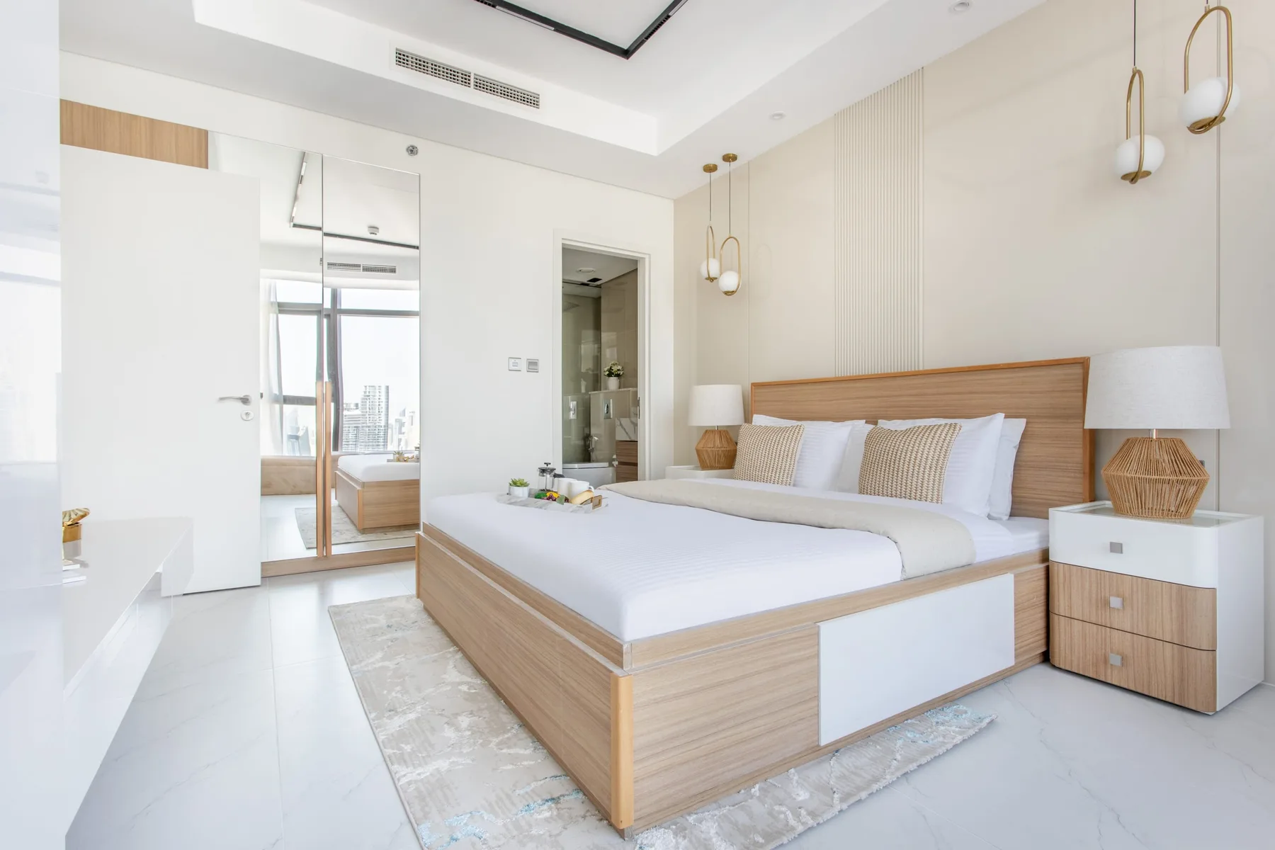 A bright bedroom with a large bed, bedside tables, and mirrored wardrobe doors.