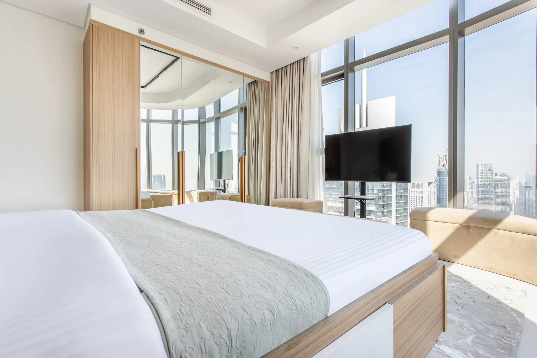 A bright bedroom with a large bed, floor-to-ceiling windows, and a television.