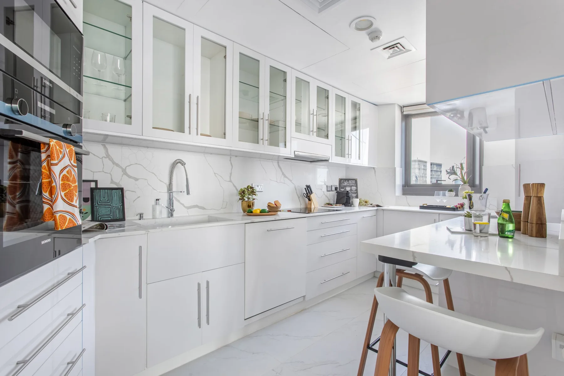 A bright white kitchen with glass-front cabinets and a central island.