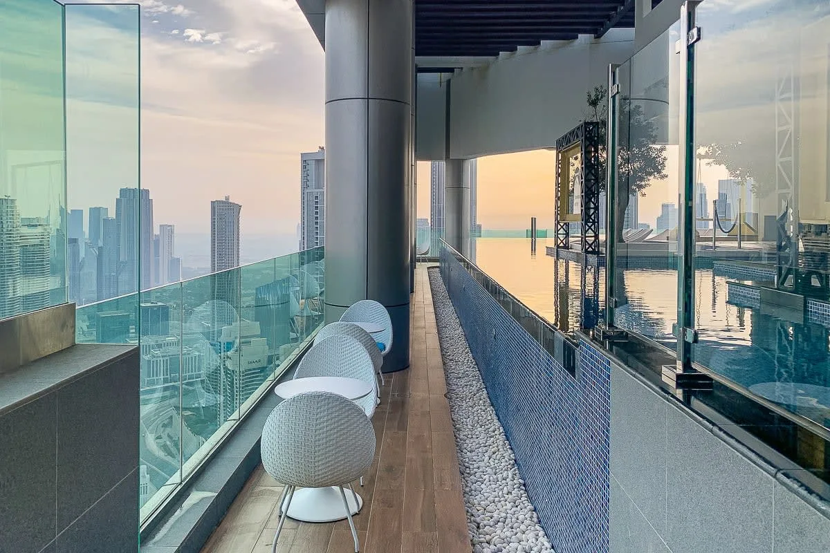 A rooftop poolside terrace has glass railings and seating overlooking the city.