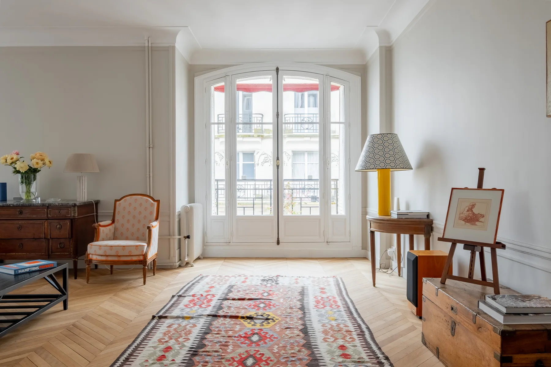 A bright living room with tall windows, seating, and a patterned rug.