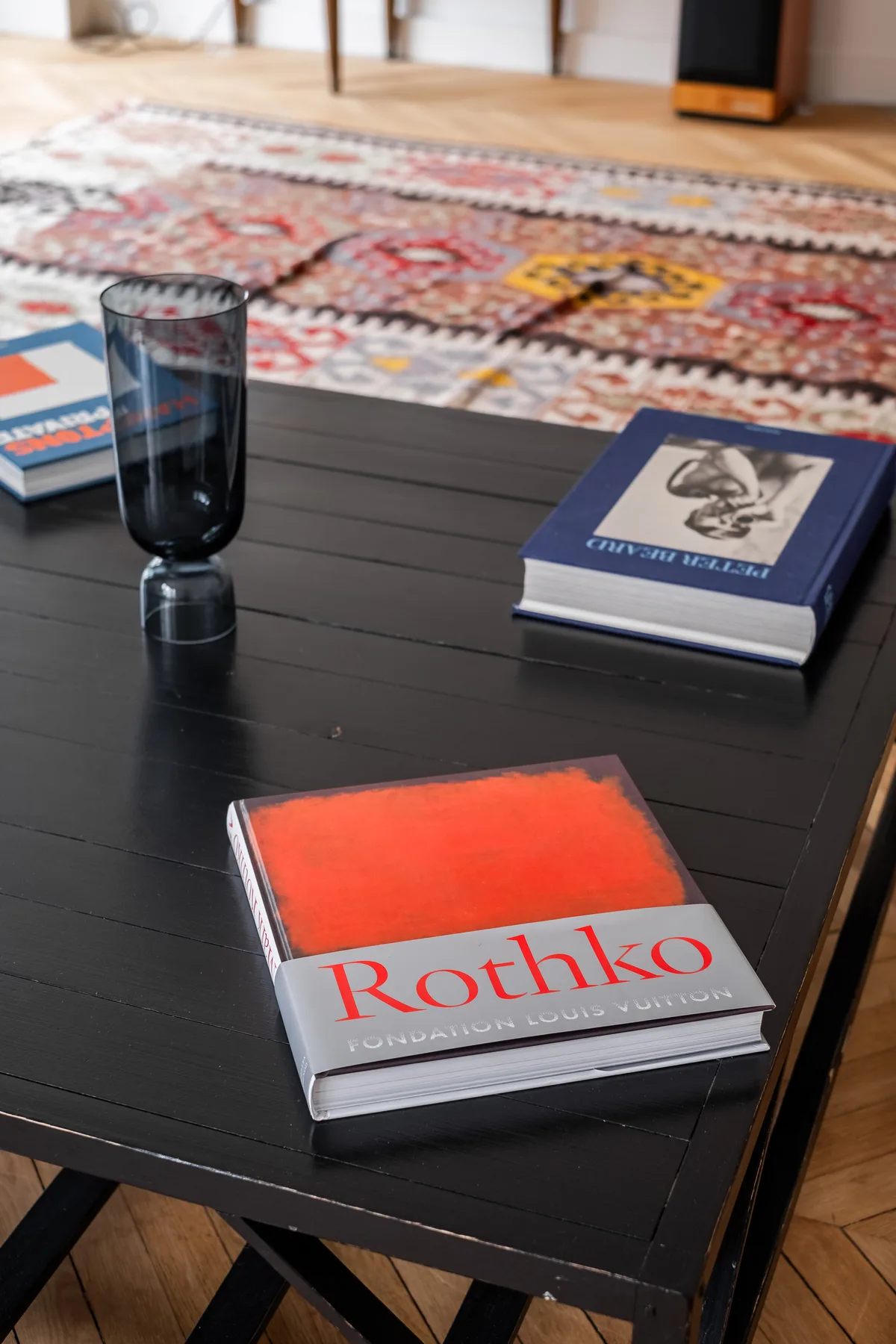 An art book and other books sit on a black coffee table beside a patterned rug.