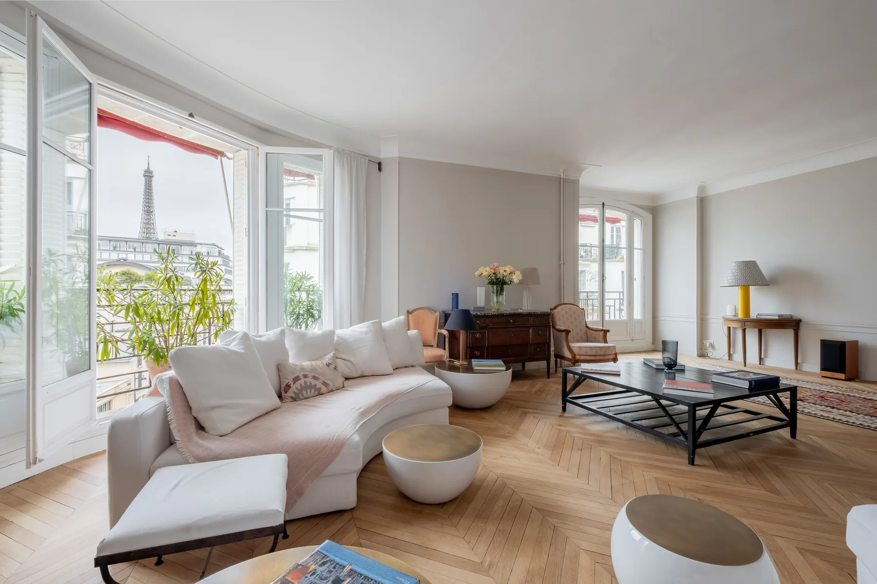 A bright living room with seating, a coffee table, and tall windows overlooking the Eiffel Tower.