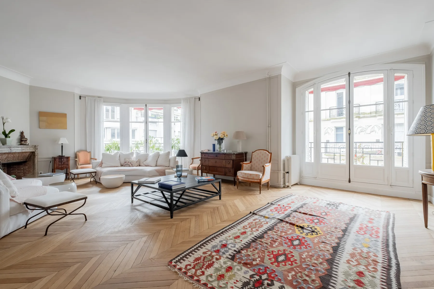 A bright living room with large windows, seating, and a patterned rug.
