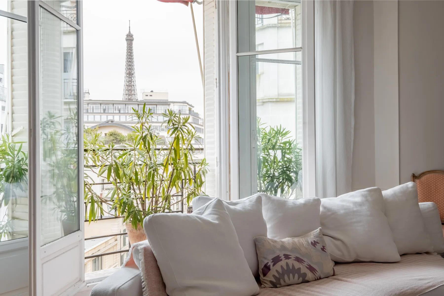 A bright living room with cushioned seating, potted plants, and a view of the Eiffel Tower.