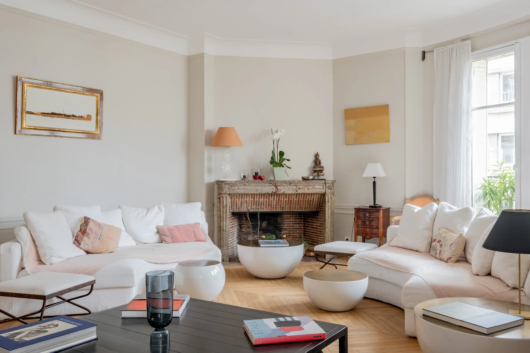 A bright living room with pale seating arranged around a fireplace.