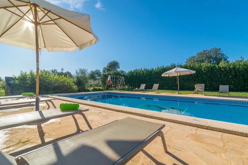 An outdoor swimming pool is surrounded by sun loungers and large umbrellas.