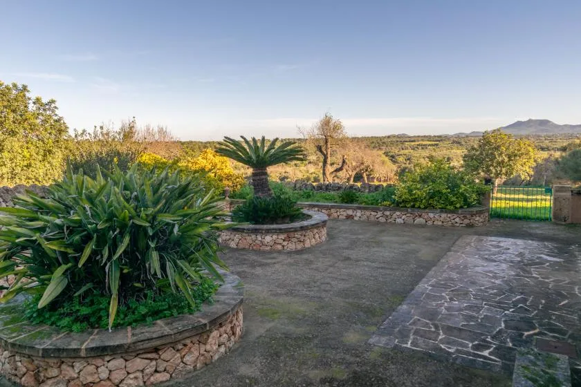 A paved garden courtyard with leafy plants and distant hills.