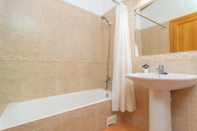 A tiled bathroom with a bathtub, shower curtain, and pedestal sink.