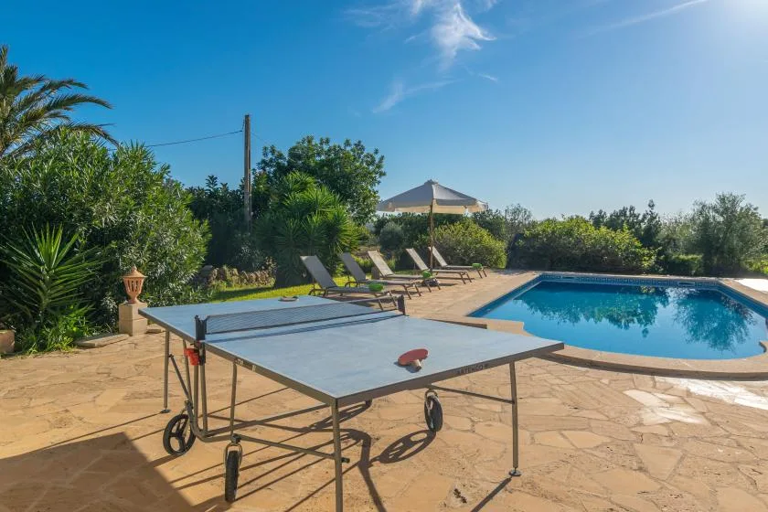 A sunlit outdoor pool area with a ping-pong table and lounge chairs.