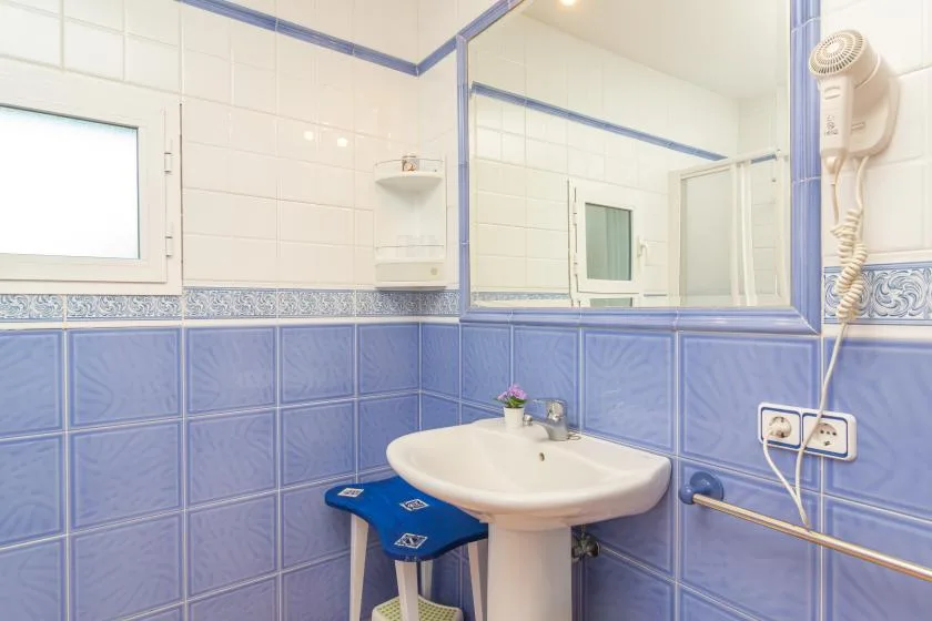 A tiled bathroom with a sink, mirror, and wall-mounted hair dryer.