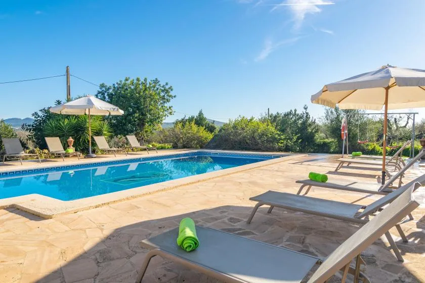An outdoor pool beside a paved deck with loungers and umbrellas.