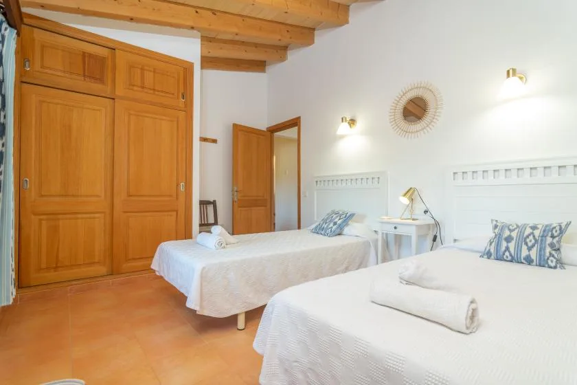 A bright bedroom with two beds and exposed wooden ceiling beams.