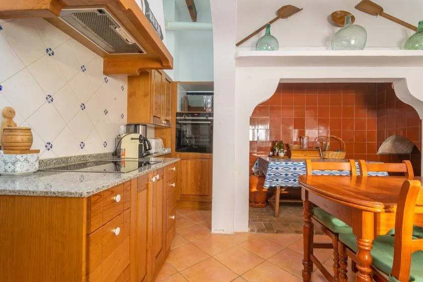 A tiled kitchen with wooden cabinets opens onto a dining area with a wooden table.