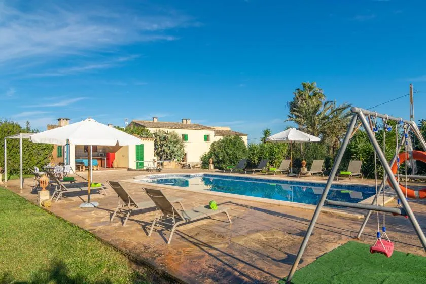 Outdoor pool area with deck seating and a swing set beside a house.