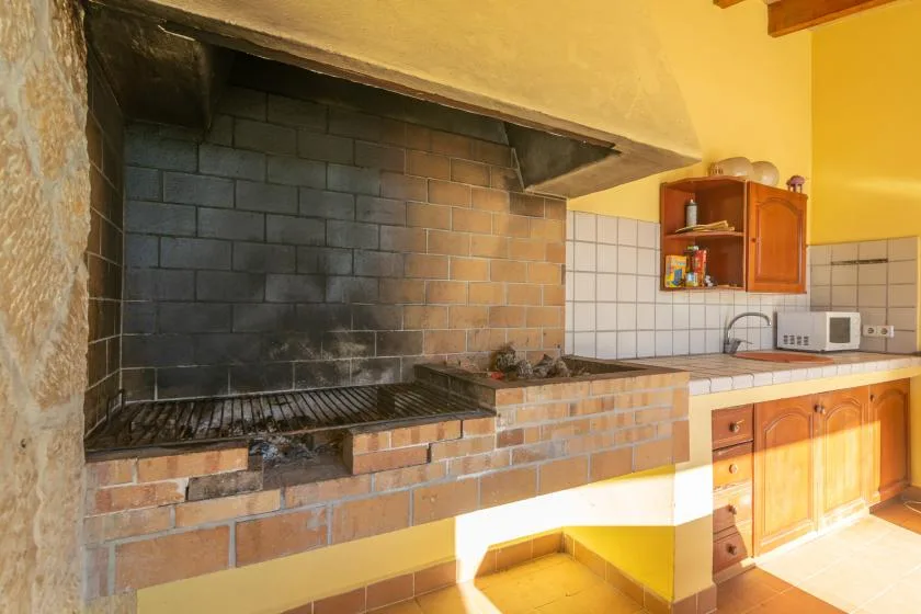 A brick barbecue grill sits beside a tiled kitchen counter and wooden cabinets.