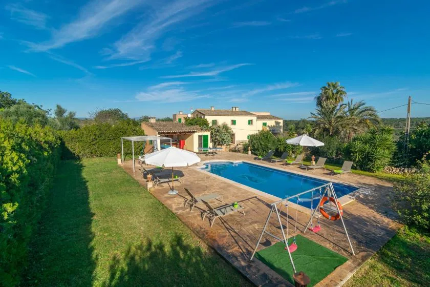 An outdoor swimming pool beside a house, with loungers and garden greenery.