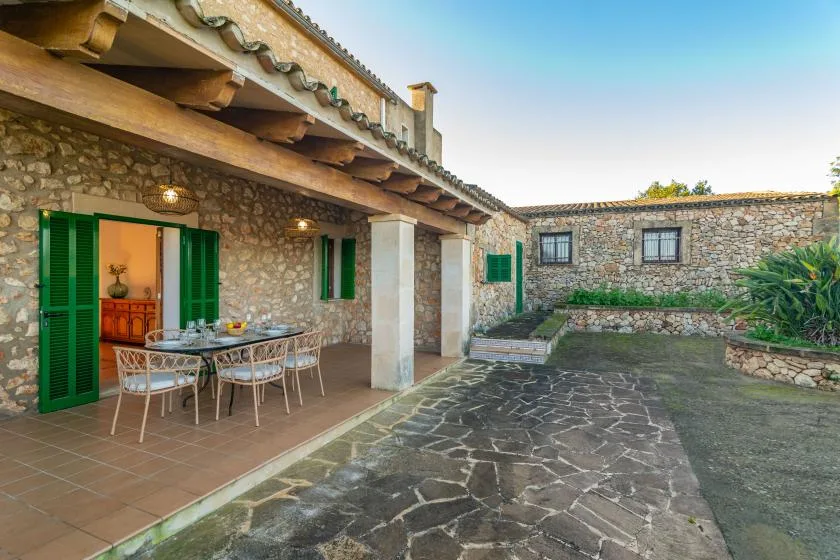A stone courtyard with a covered patio, outdoor dining table, and green shutters.