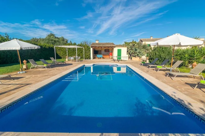 A swimming pool is surrounded by a paved patio with loungers and umbrellas.