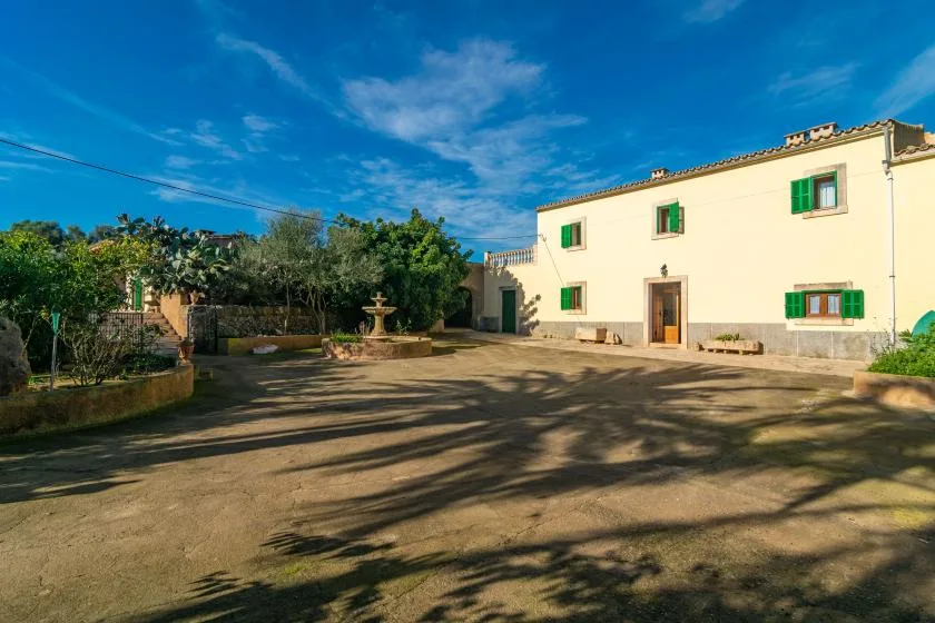 A sunlit courtyard in front of a pale building with green shutters.