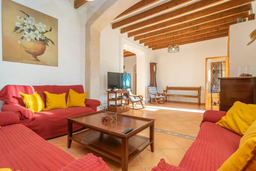 A living room with red seating, a wooden coffee table, and exposed ceiling beams.